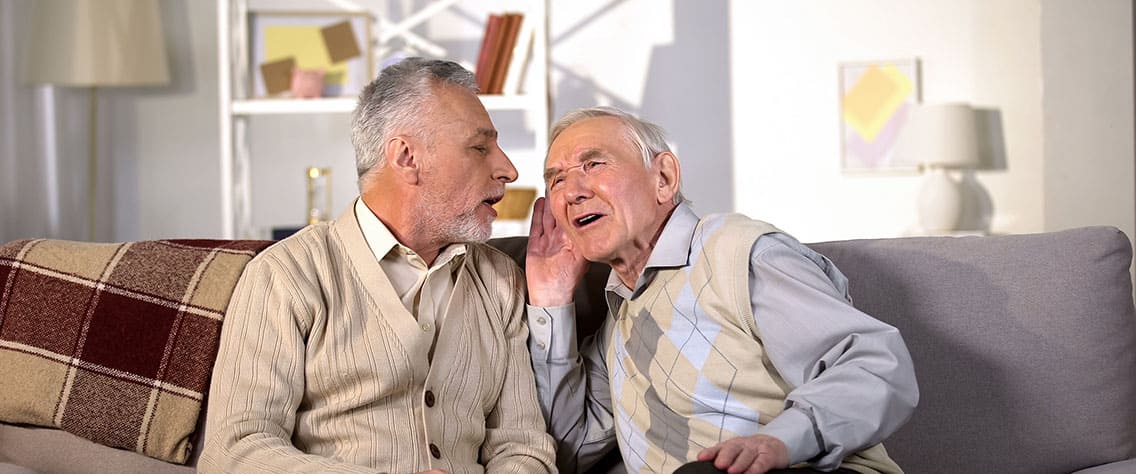 Old man talking to friend with hearing loss sitting on sofa at home.