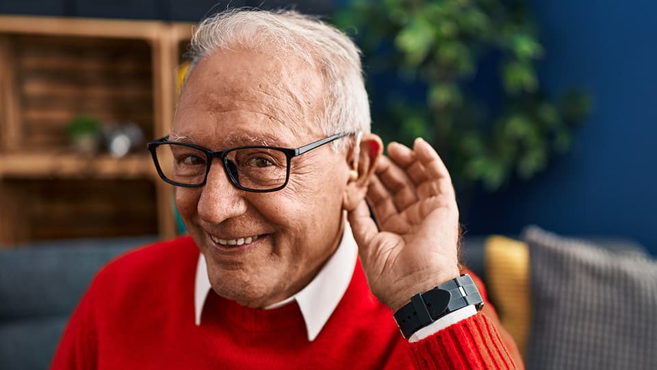 Senior man with hearing loss smiling confident using hearing aid at home